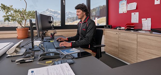 Ein Mann arbeitet an einem Schreibtisch im Büro mit Blick auf schneebedeckte Berge durch das Fenster.